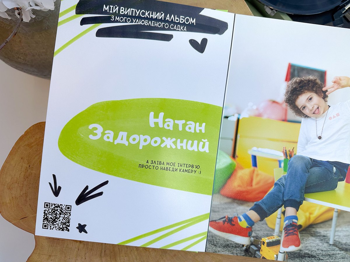 Сторінка дитини в альбомі HANDSOME — імʼя, QR-код на відеоінтервʼю та портрет хлопчика в ігровій кімнаті