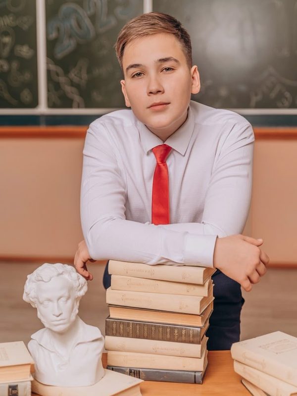 Звичайна шкільна зйомка: учень за стосом книжок біля дошки